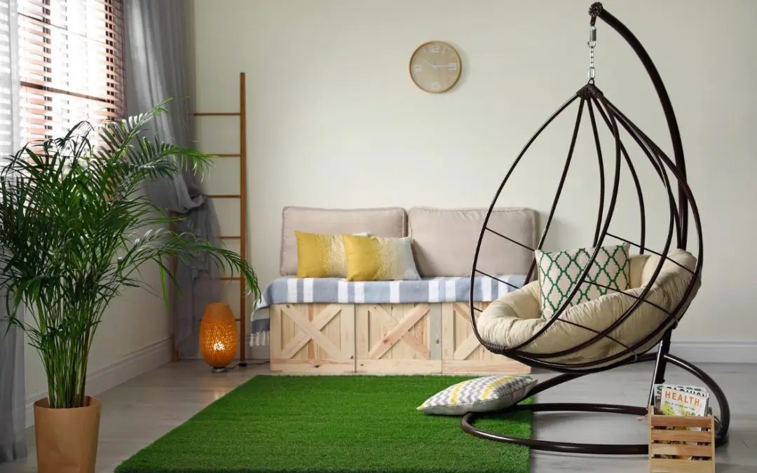 Cozy indoor living room with artificial grass rug, hanging egg chair, wooden sofa with cushions, and indoor plants for modern home décor.