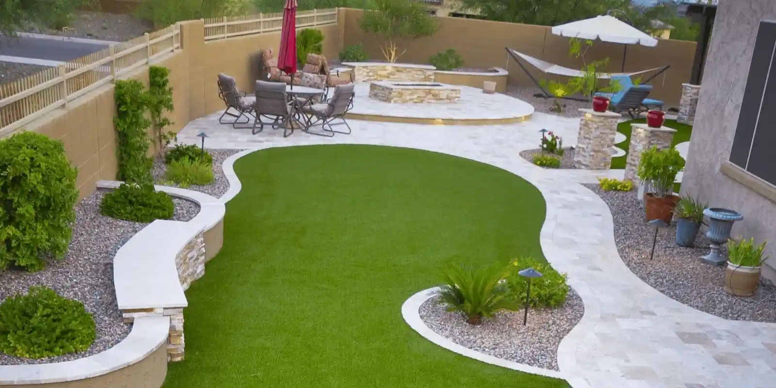 Beautiful backyard with artificial grass lawn, modern stone pathways, outdoor seating area, and landscaped plants creating a clean and low-maintenance design.