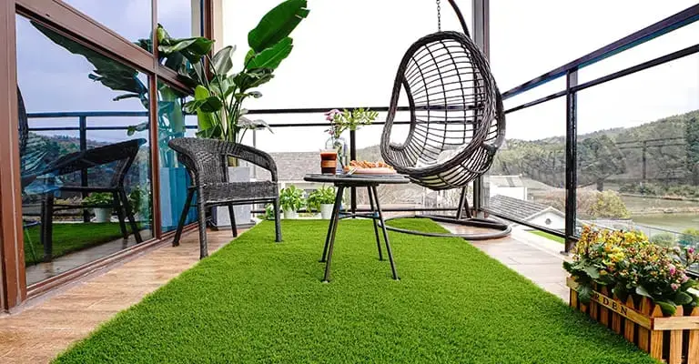   Modern balcony decorated with artificial grass flooring, hanging chair, potted plants, and outdoor seating creating a cozy green retreat.
