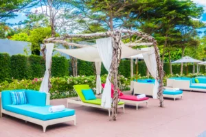 Colorful outdoor lounge chairs with canopy shades by a luxury swimming deck surrounded by greenery and flowers.
