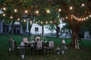 Elegant outdoor dining setup under string lights with candles, lanterns, and a beautifully decorated table in a garden setting at dusk.
