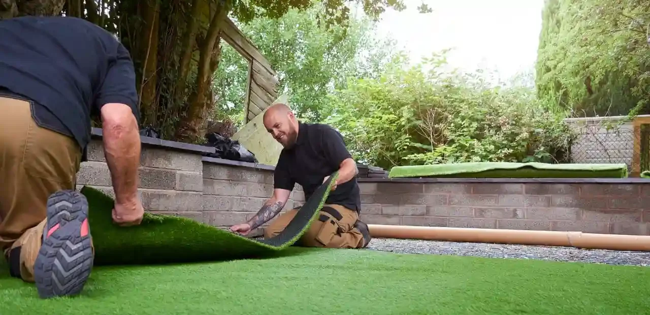 two man are installing artificial grass in yard 
