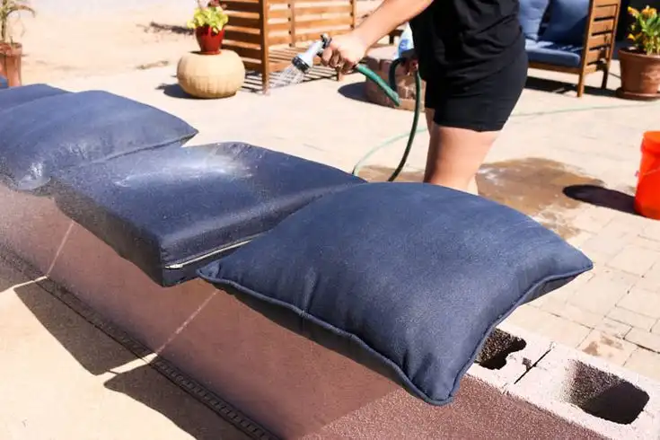 Washing outdoor patio cushions with garden hose in backyard